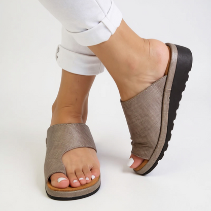 Brown open-toe sandals worn with light-colored pants on a white background