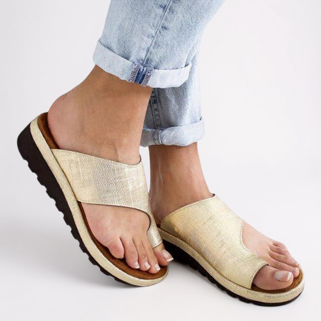 Gold sandals worn with rolled-up jeans on a light background