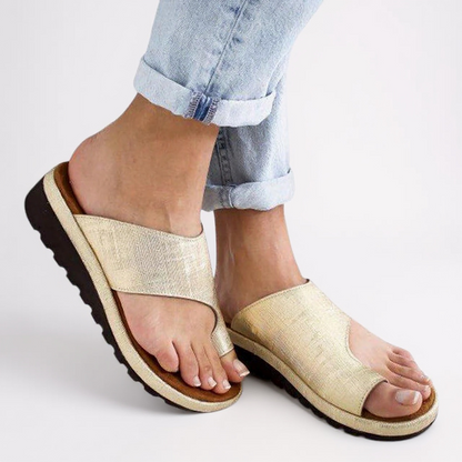 Gold sandals worn with rolled-up jeans on a light background