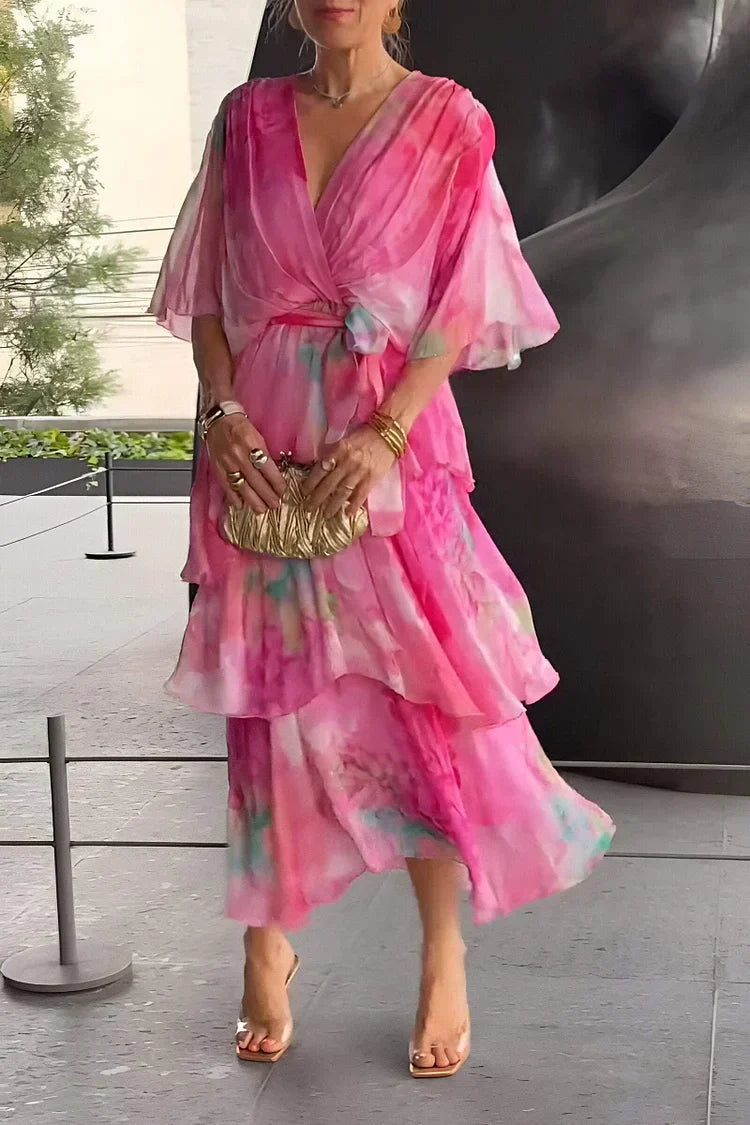 Woman in a pink floral dress holding a gold clutch against an outdoor background.