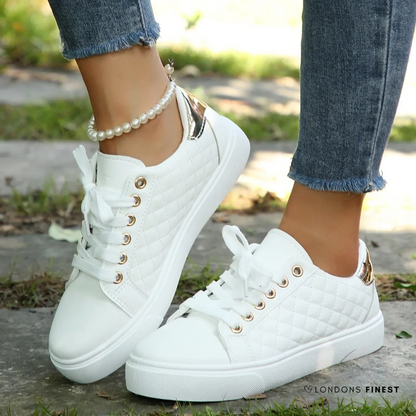 White sneakers with gold accents worn by a person on a blurred outdoor background