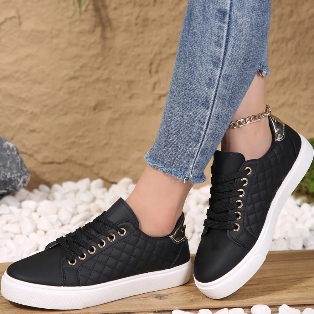 Black sneakers with white soles worn with blue jeans against a textured wall background