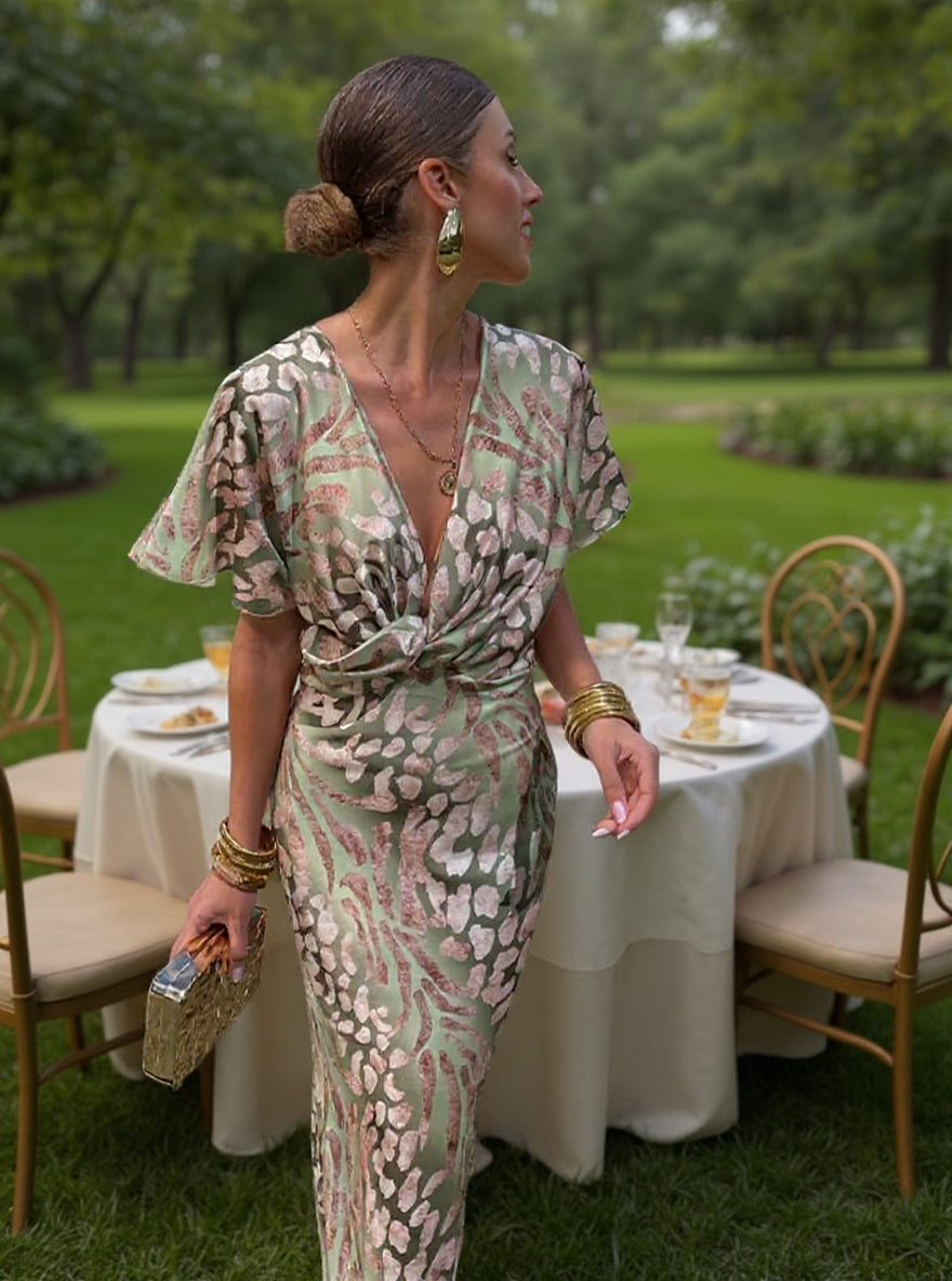Woman in a patterned dress standing outdoors near a table with a white tablecloth.