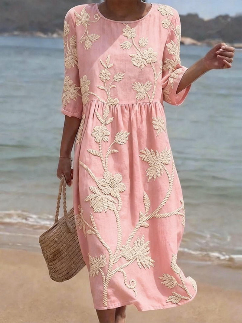 Person wearing a pink dress with floral embroidery by the beach