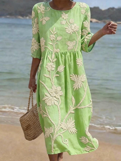 Woman wearing a green dress with white floral embroidery on a beach.