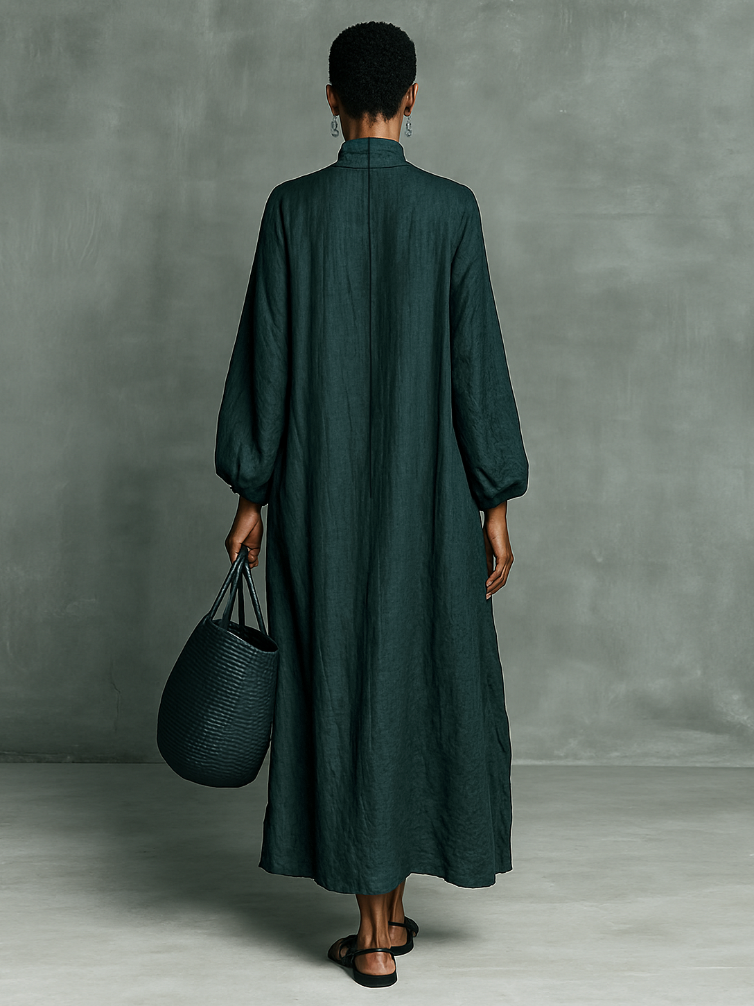 Person wearing a long dark green dress holding a matching bag against a gray background