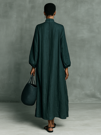 Person wearing a long dark green dress holding a matching bag against a gray background