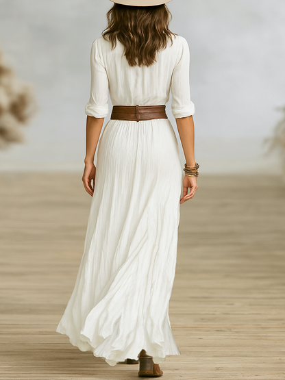 Woman wearing a long white dress with a brown belt on a wooden floor.