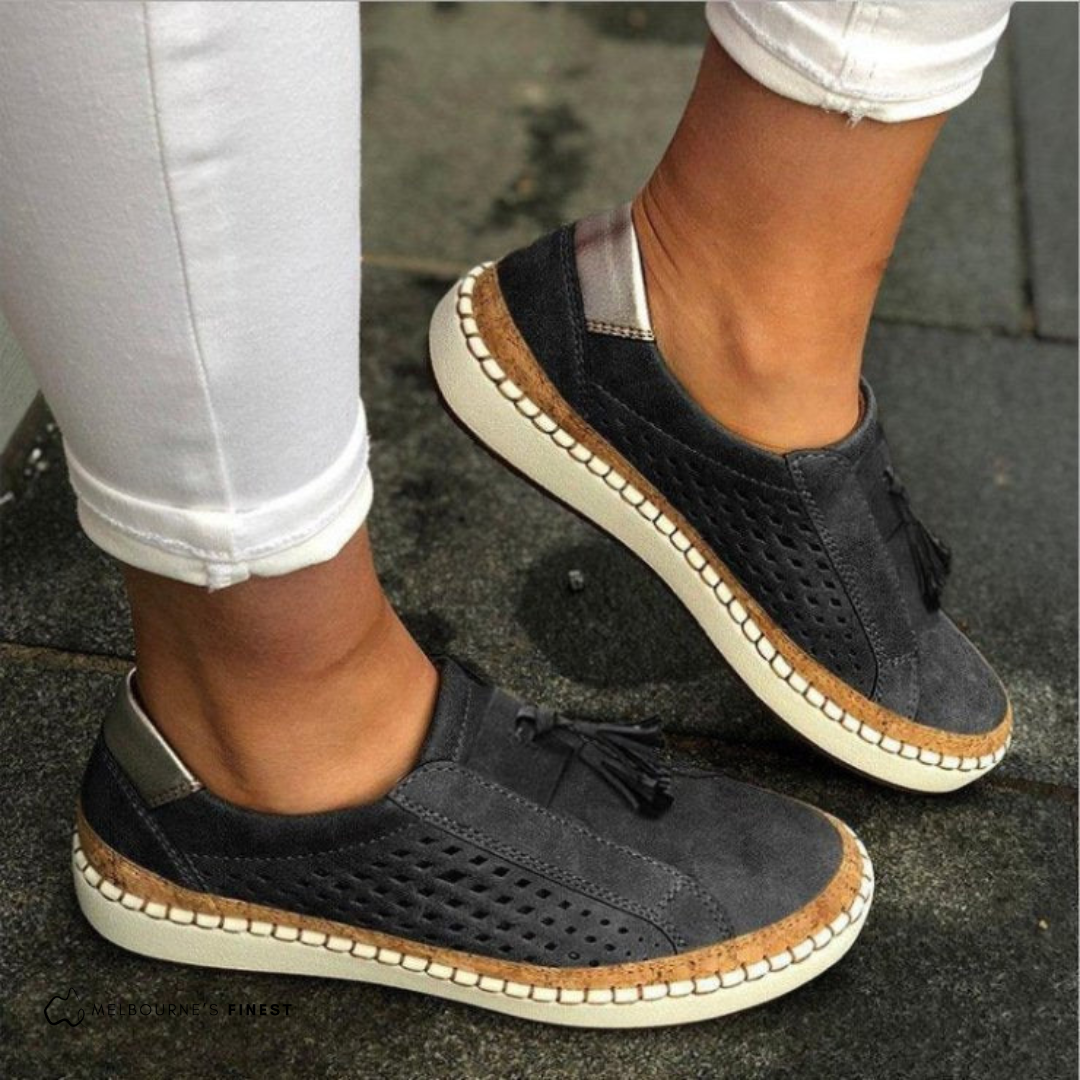 Black casual shoes with brown accents worn by a person on a pavement.