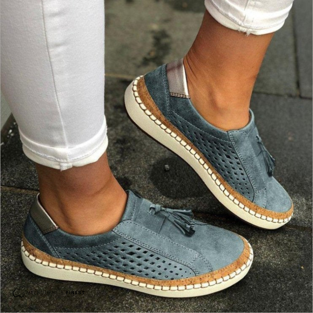 Blue suede shoes with brown accents worn on a pavement.