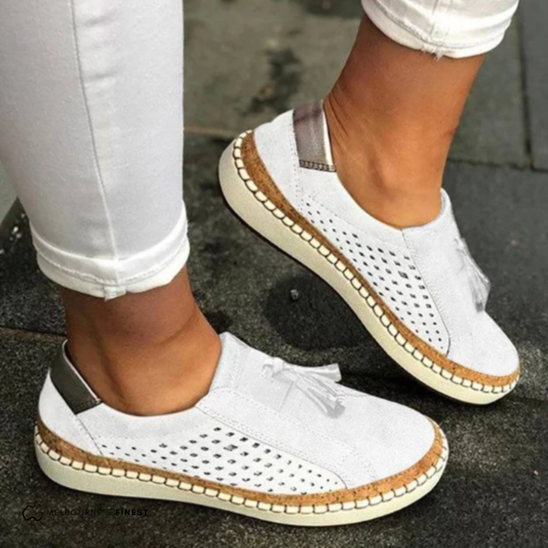 White sneakers with brown accents worn by a person on a dark surface