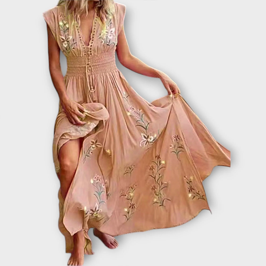 Woman wearing a long, flowing dress with floral embroidery on a plain background