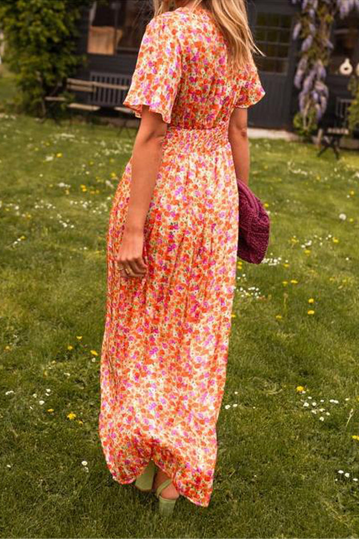 Woman in a floral dress standing on grass with flowers.