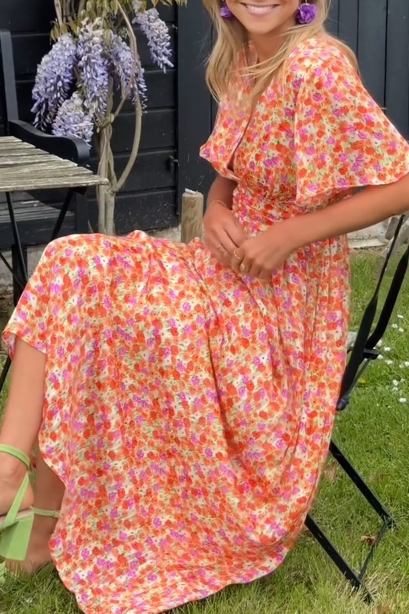 Woman wearing a colorful floral dress sitting outdoors.