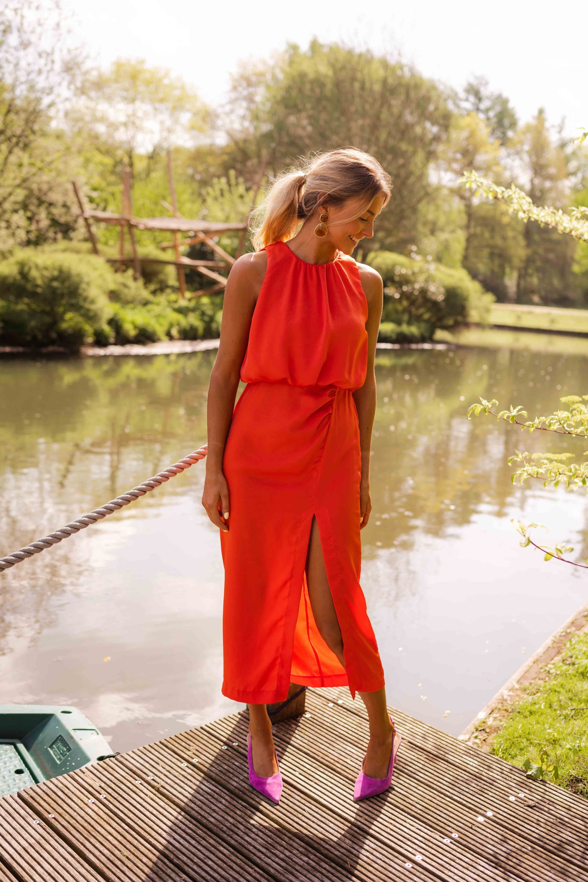 Woman in a bright orange dress standing on a dock by a lake