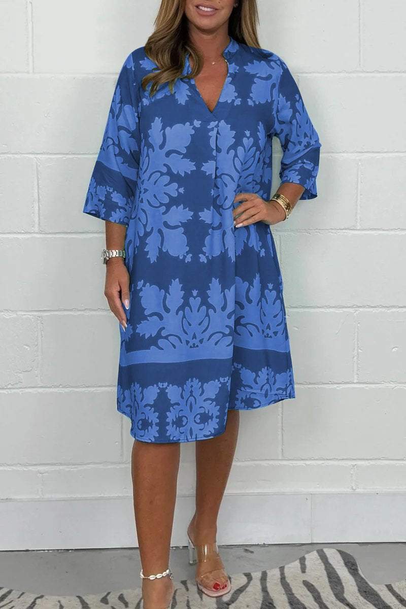 Woman wearing a blue floral dress against a white brick wall.