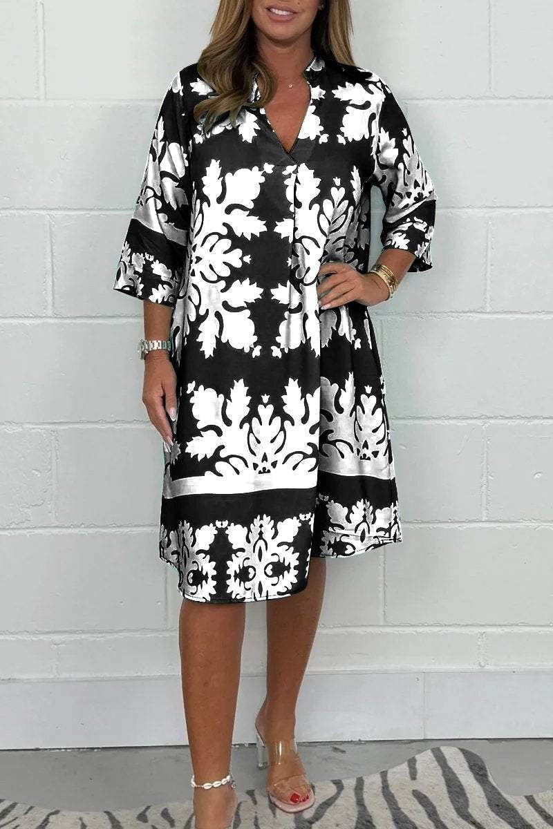 Woman wearing a black and white patterned dress against a white brick wall.