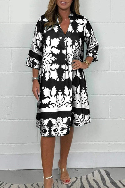 Woman wearing a black and white patterned dress against a white brick wall.