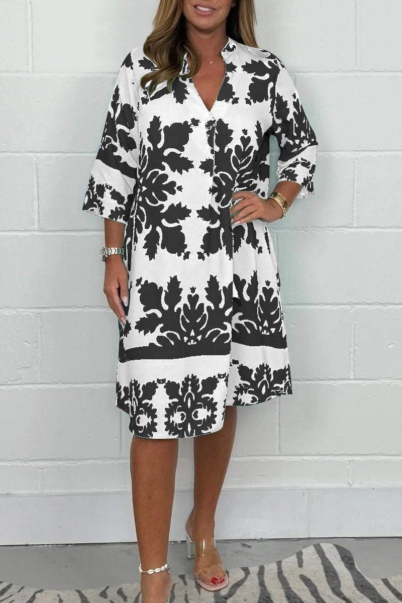 Woman wearing a black and white floral dress against a white brick wall.