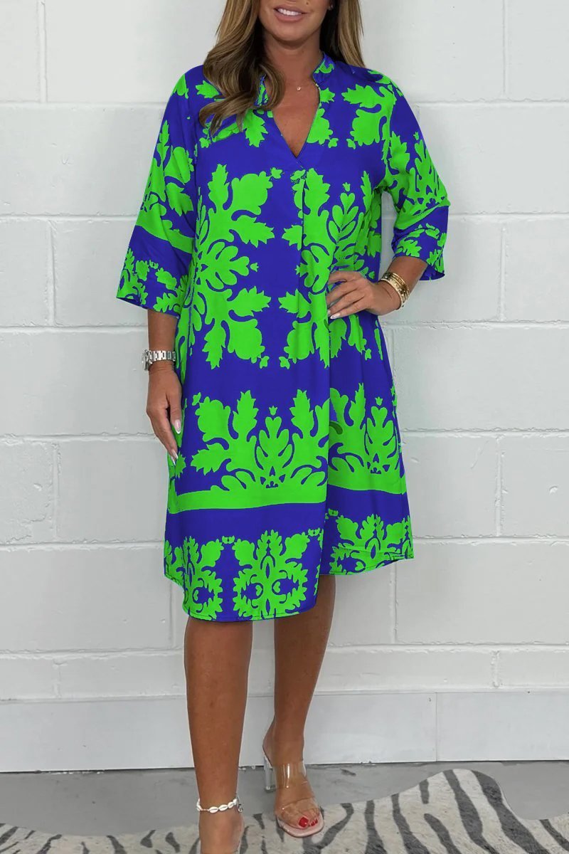 Woman wearing a blue and green patterned dress against a white brick wall.