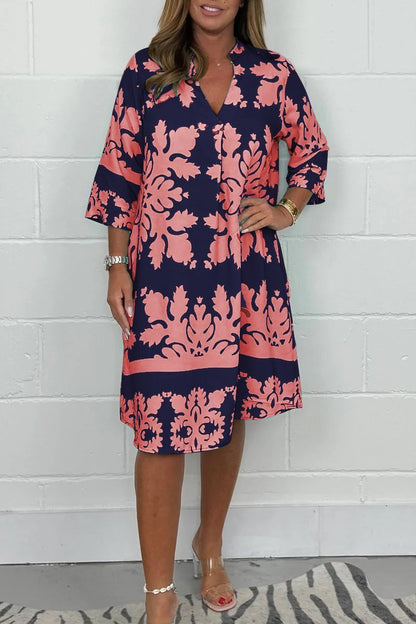 Woman wearing a navy and pink floral dress against a white brick wall.
