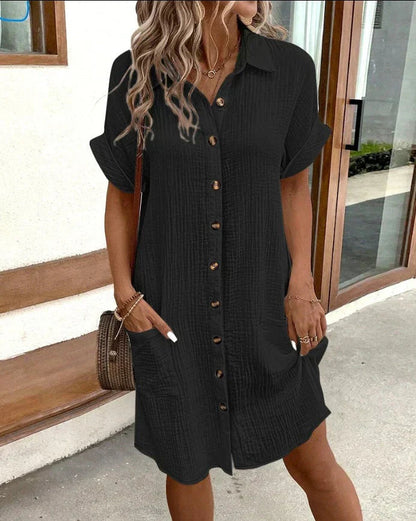 Woman wearing a black button-up dress standing outdoors.