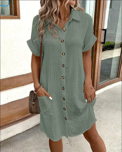 Woman wearing a green dress with buttons, standing on a sidewalk.