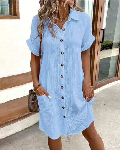 Woman wearing a light blue dress with buttons, standing outdoors.