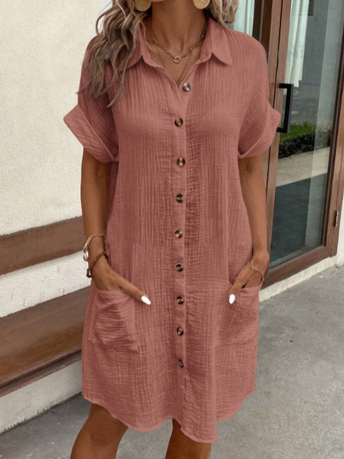 Woman wearing a pink button-up dress standing outdoors.