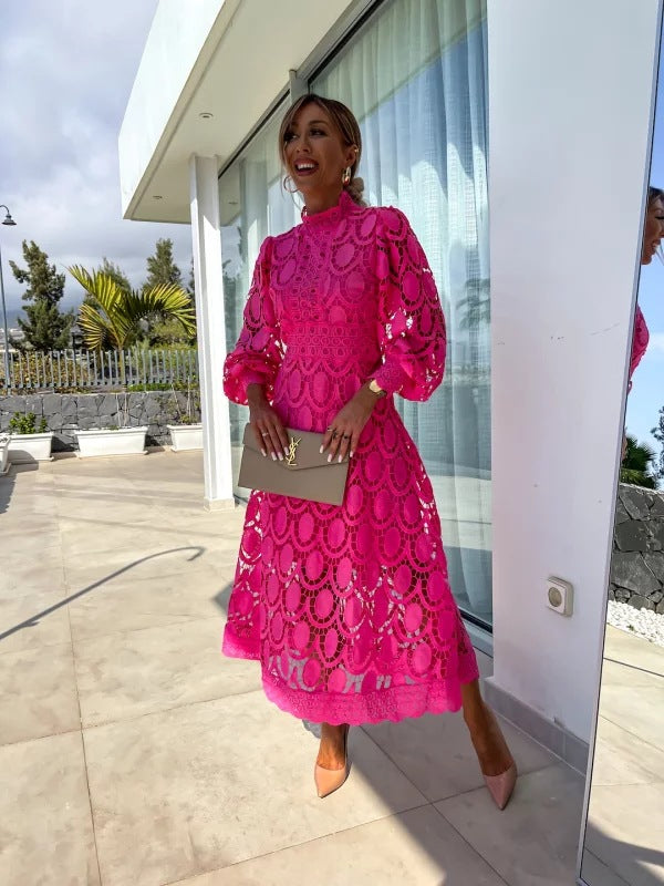 Woman in a bright pink dress standing in front of a modern building with glass doors.