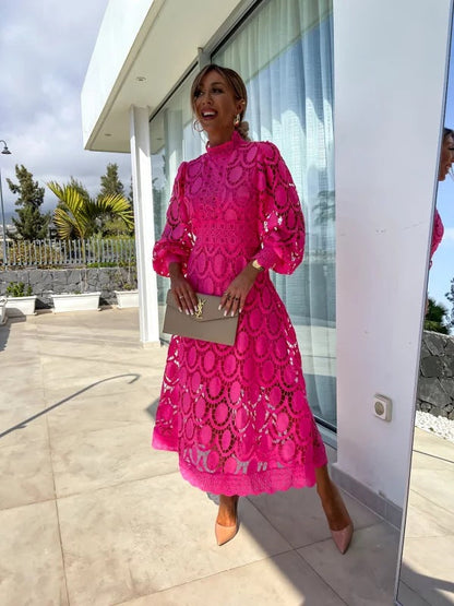 Woman in a bright pink dress standing in front of a modern building with glass doors.