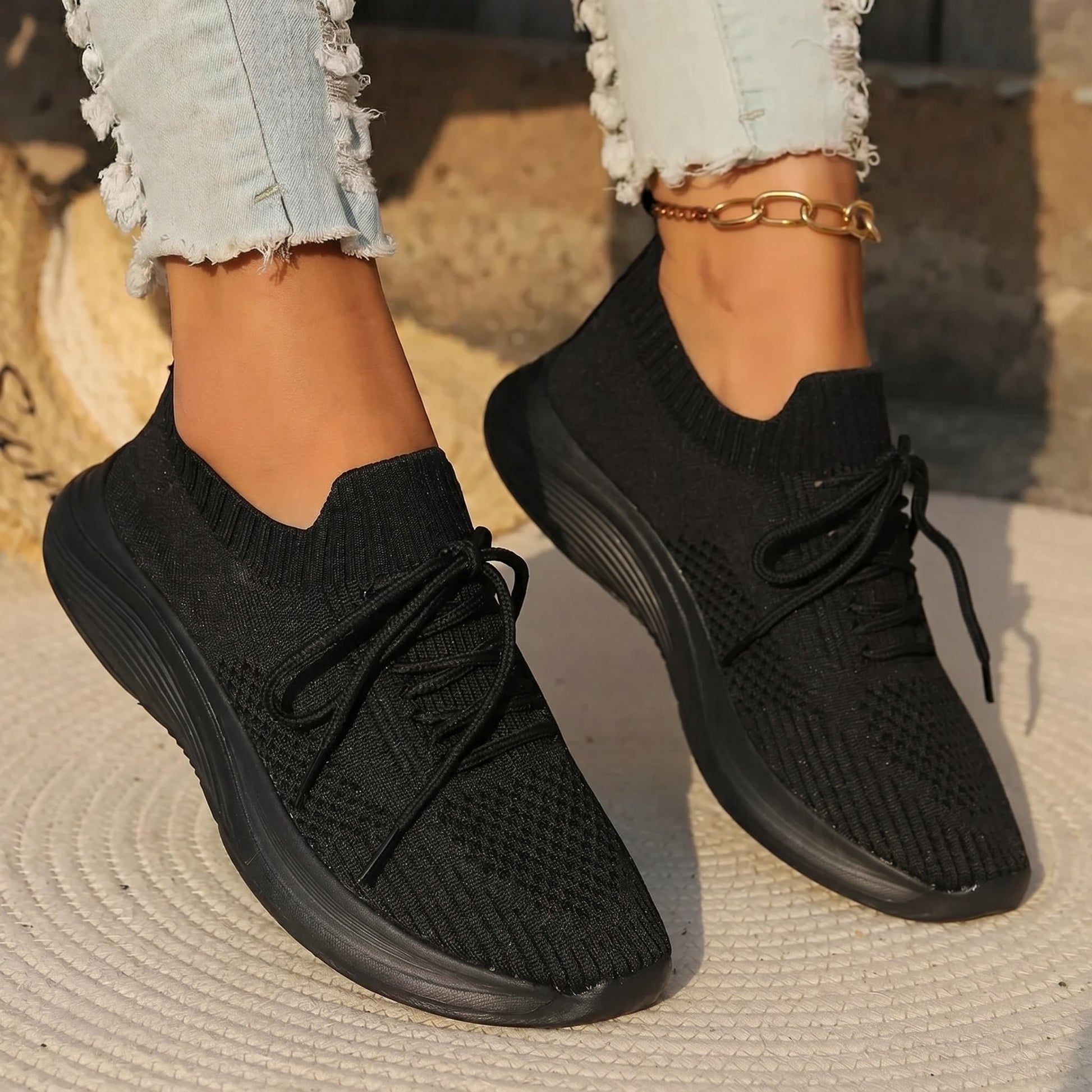 Black knit sneakers worn with light blue jeans on a textured surface.