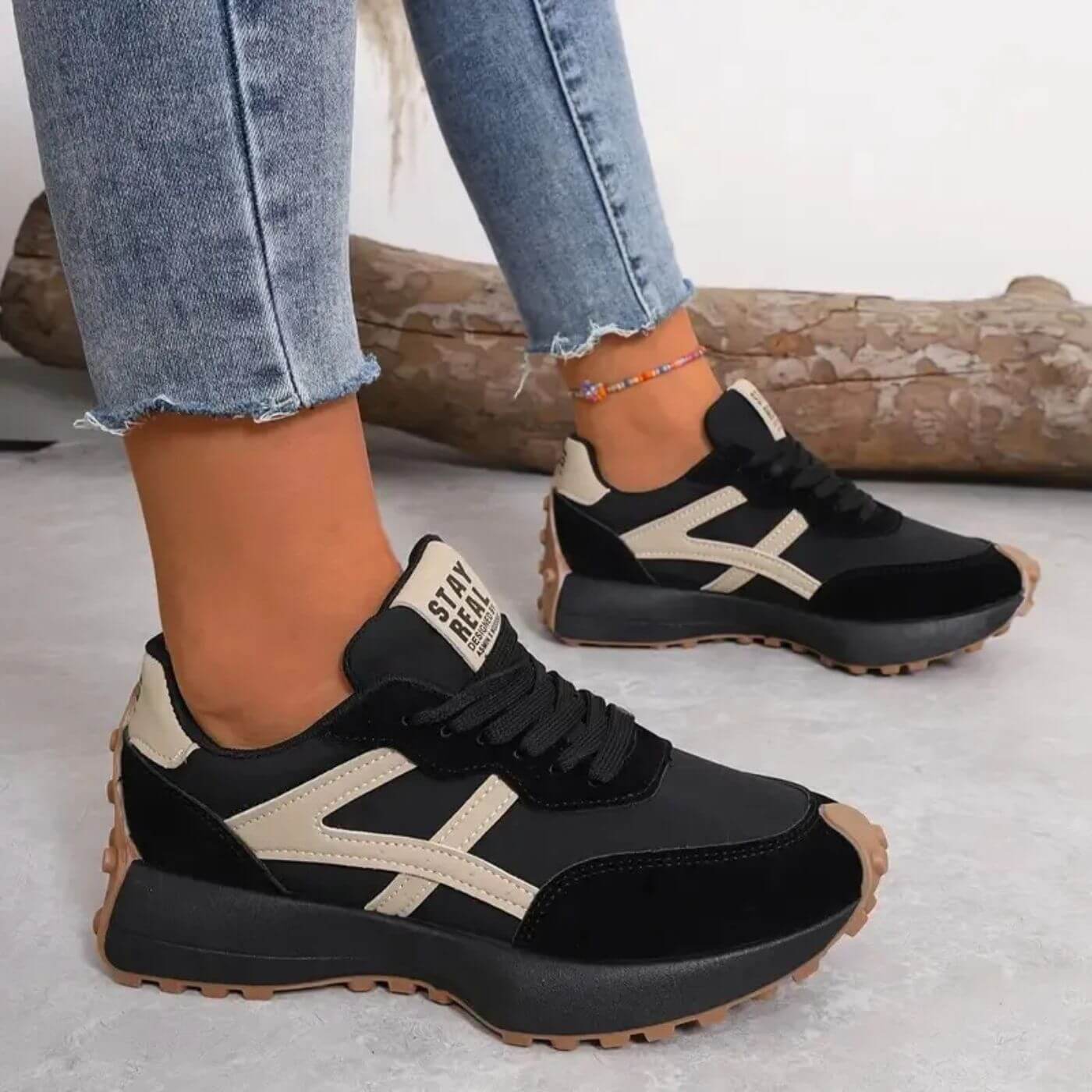Black and beige sneakers worn with light blue jeans on a neutral background