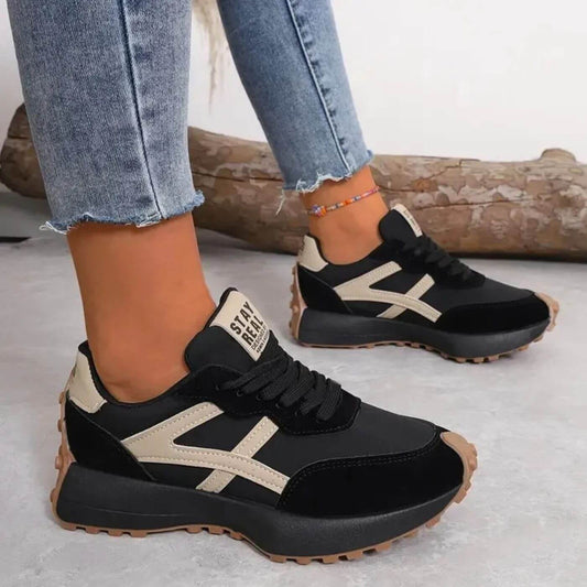Black and beige sneakers worn with light blue jeans on a neutral background