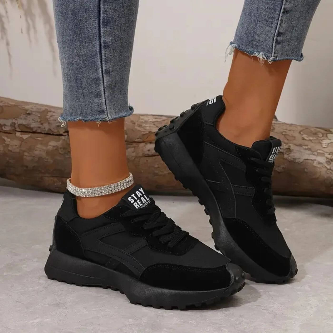Black sneakers worn with light blue jeans on a neutral background