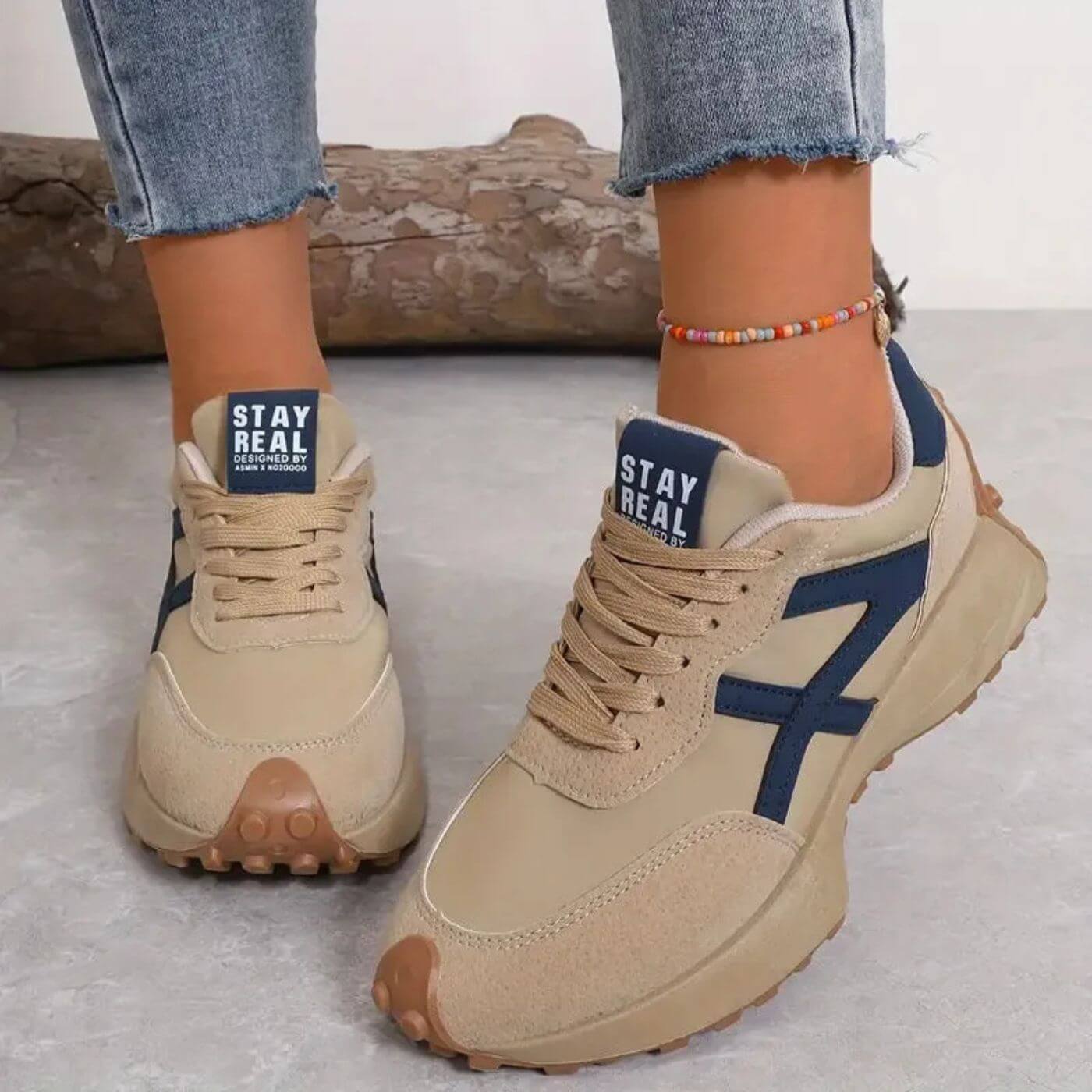 Beige sneakers with blue accents worn by a person, on a light gray background.