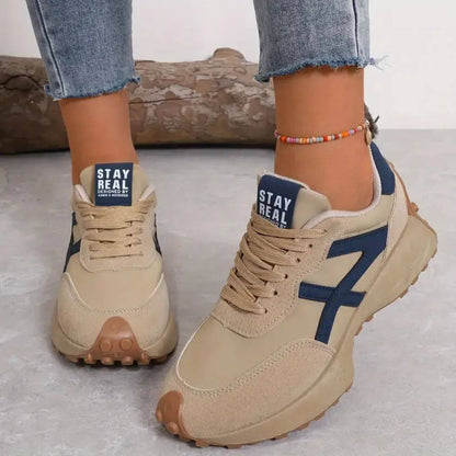 Beige sneakers with blue accents worn by a person, on a light gray background.