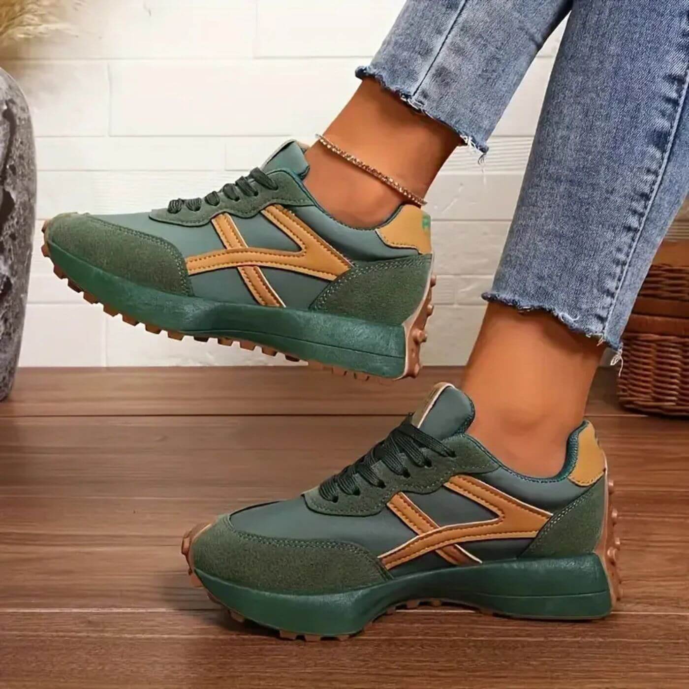 Green and brown sneakers worn with blue jeans on a wooden floor.