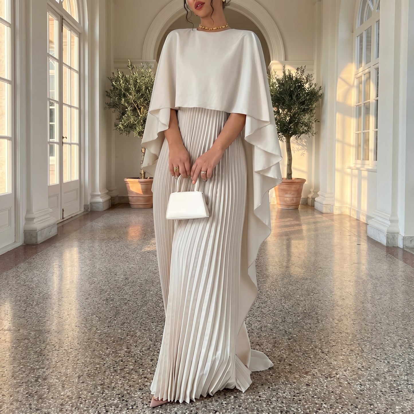 Woman in a white pleated dress with a cape in a sunlit room.