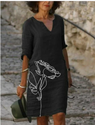 Woman wearing a black dress with a white floral design, standing against a stone wall.