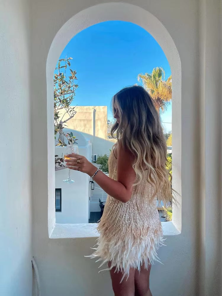 Woman in a fringed dress holding a glass of wine, standing in front of an archway with a clear blue sky.