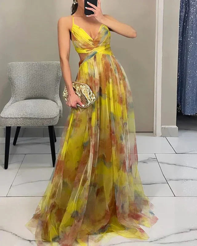 Woman wearing a yellow floral dress holding a gold clutch in a room with a chair and door.