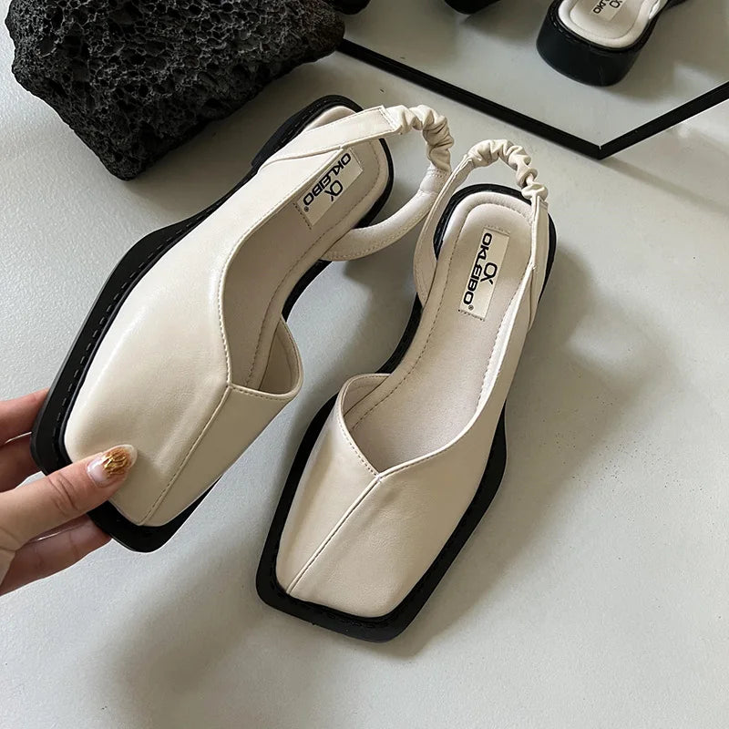 Pair of white sandals with black soles on a light surface