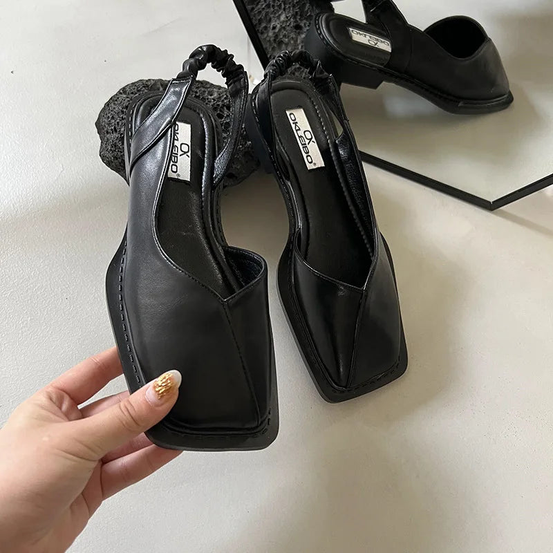 Black high-heeled shoes with a hand holding one shoe on a light background