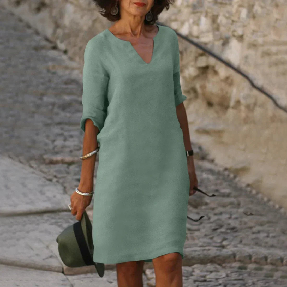 Woman wearing a green dress standing on a stone path with a stone wall background