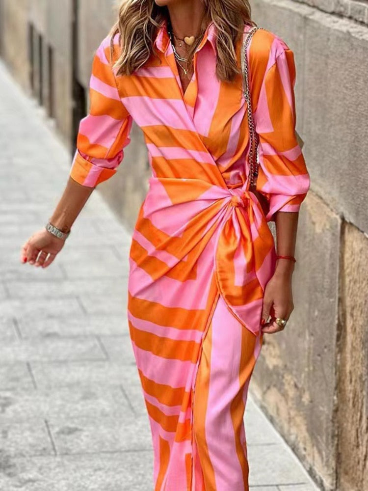 Person wearing a pink and orange striped dress walking on a sidewalk.