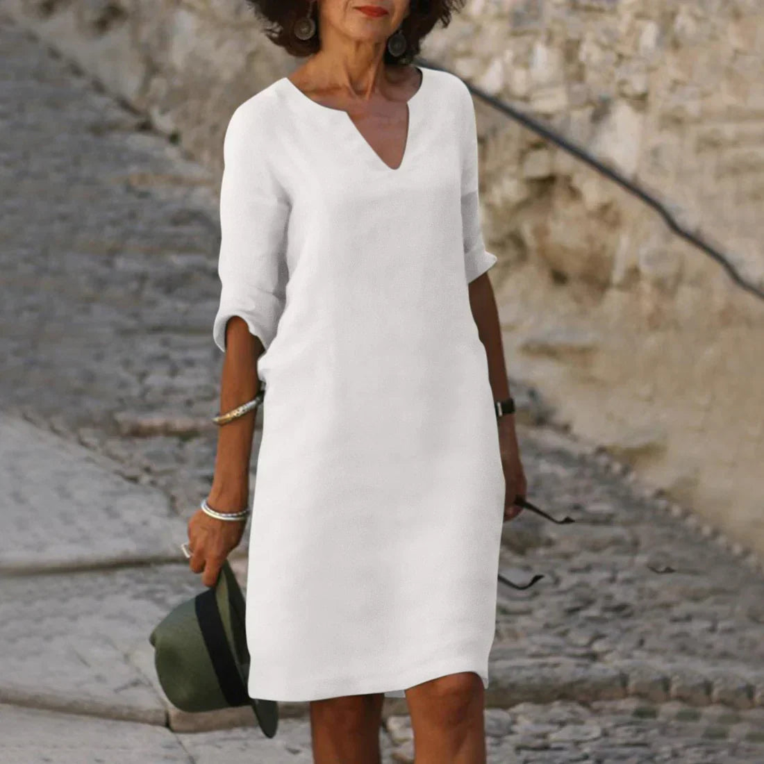 Woman wearing a white dress standing on a stone path with a stone wall background