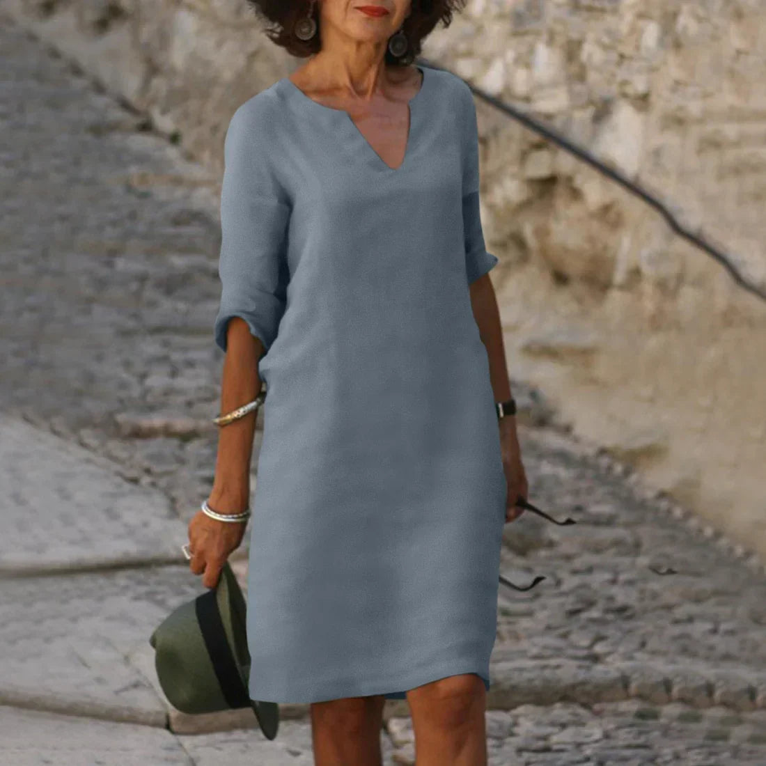 Woman wearing a blue dress standing on a stone path with a stone wall in the background