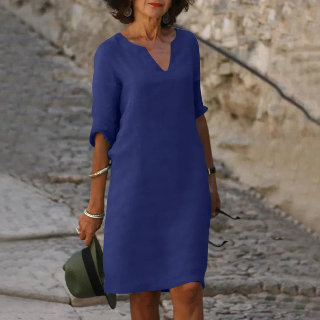Woman wearing a blue dress standing on a stone path with a stone wall in the background
