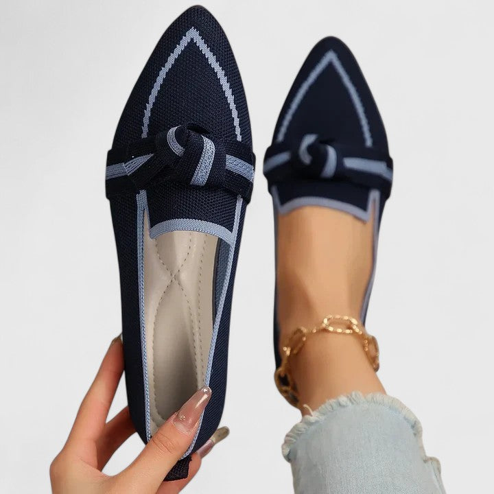 Navy blue loafers with a bow detail held by a hand on a light gray background
